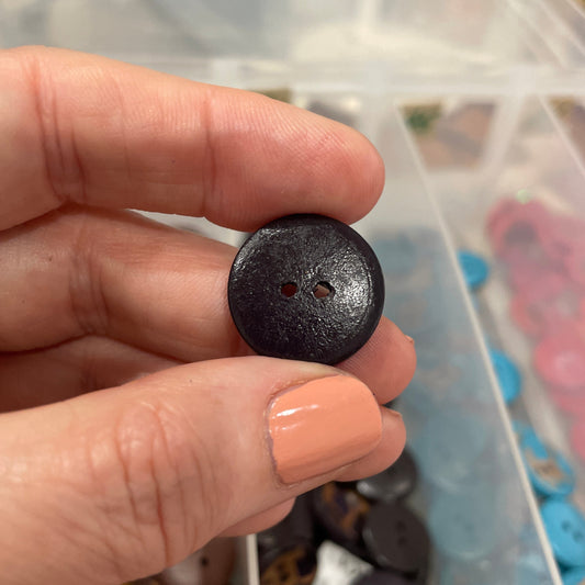 Hand holding a black button with a clear container of buttons in the background