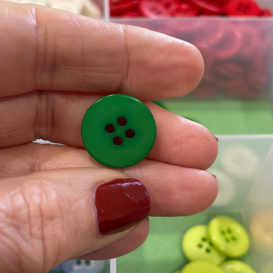Hand holding a green button with a container of colorful buttons in the background