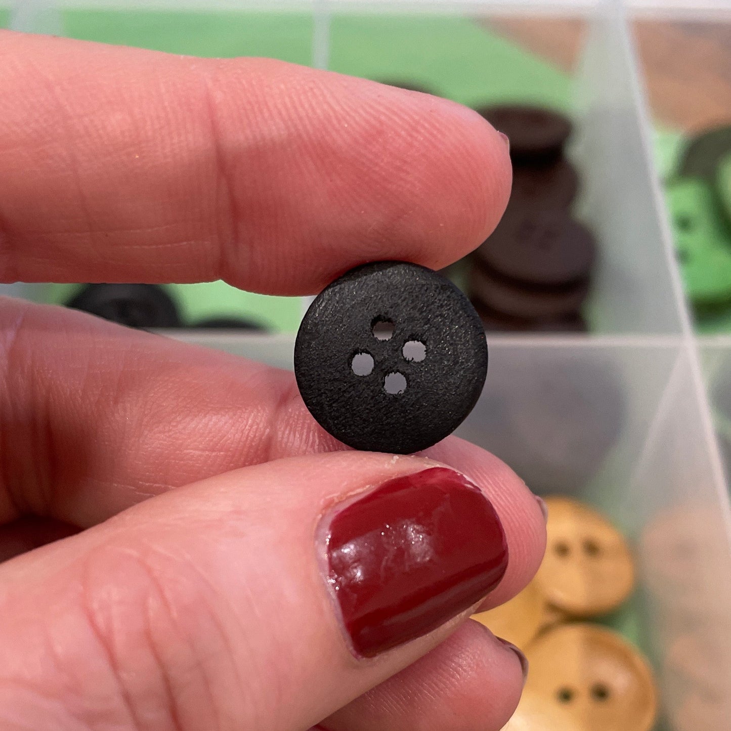 Hand holding a black button with a container of buttons in the background
