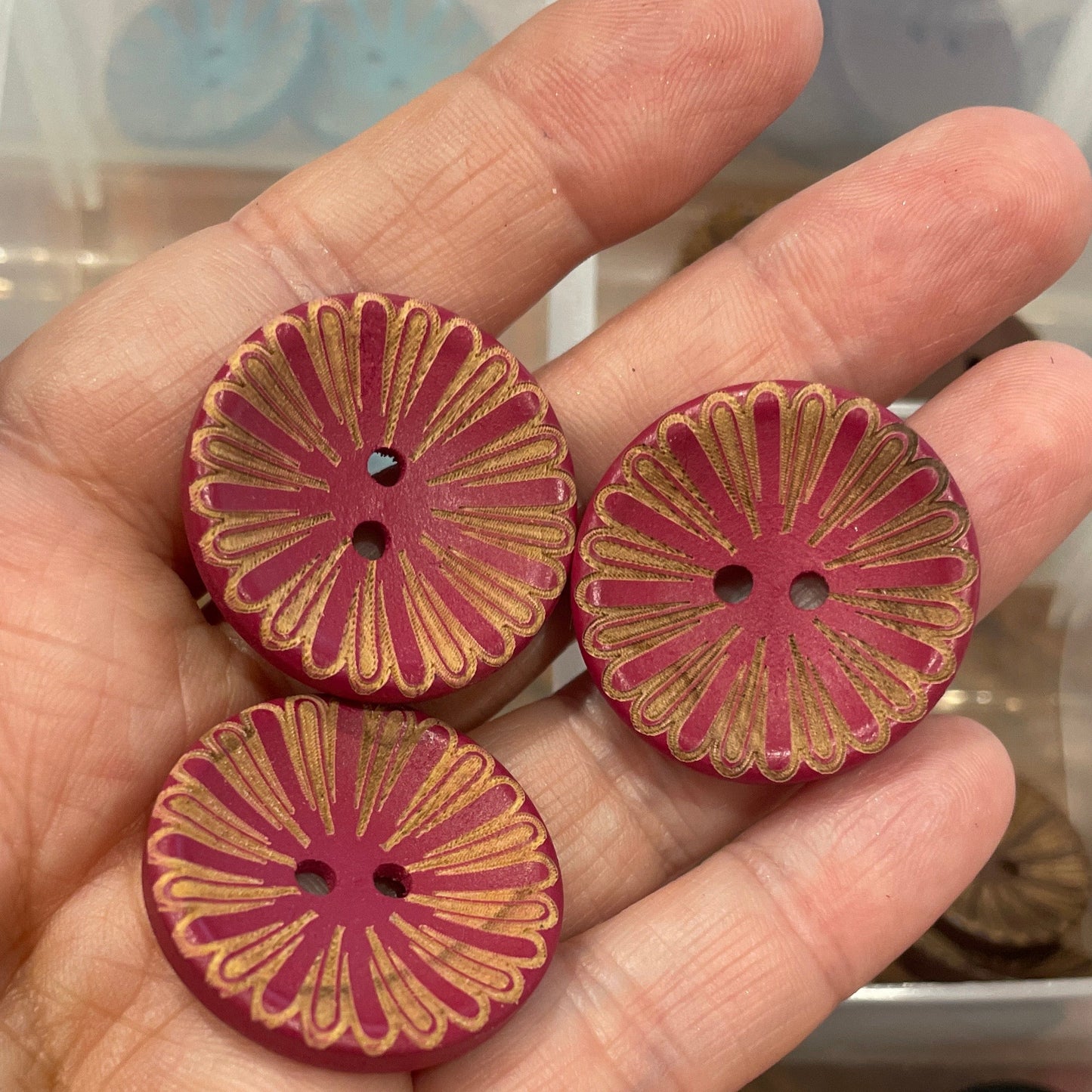 Hand holding three decorative buttons with a button collection box in the background