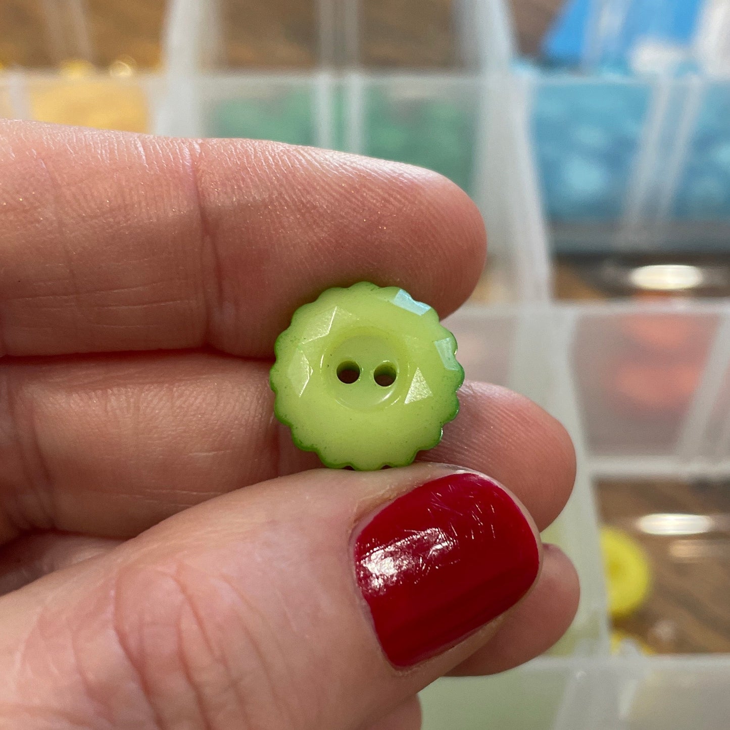 Hand holding a green button with two holes, with a background of button containers.