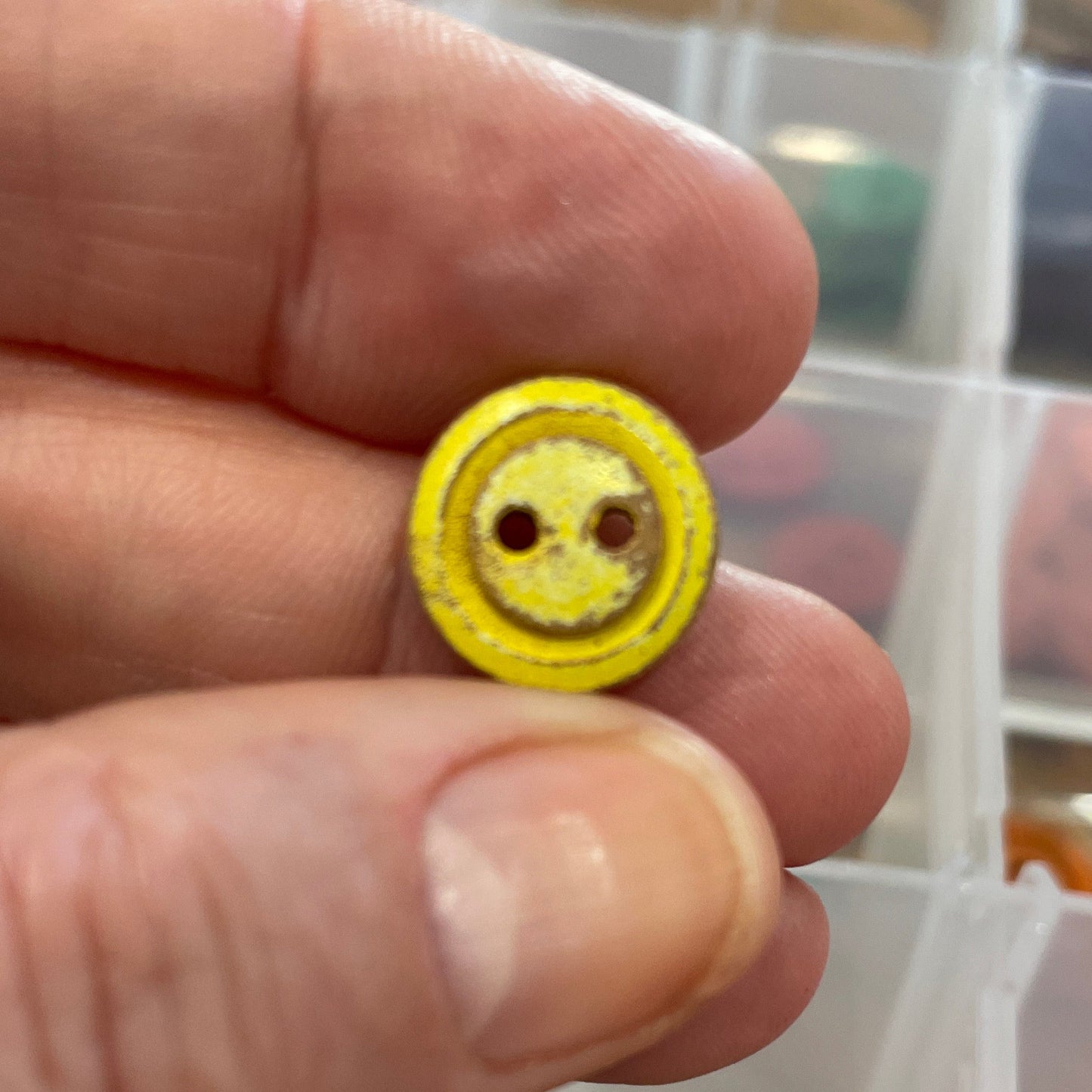 Yellow button held between fingers with a container of buttons in the background