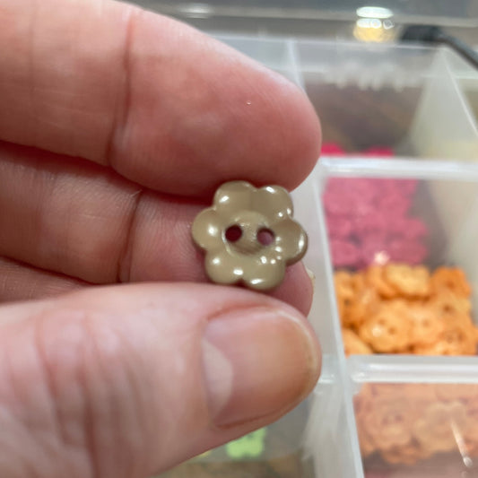 Hand holding a small gold flower-shaped object with a blurred background of a storage container with compartments.