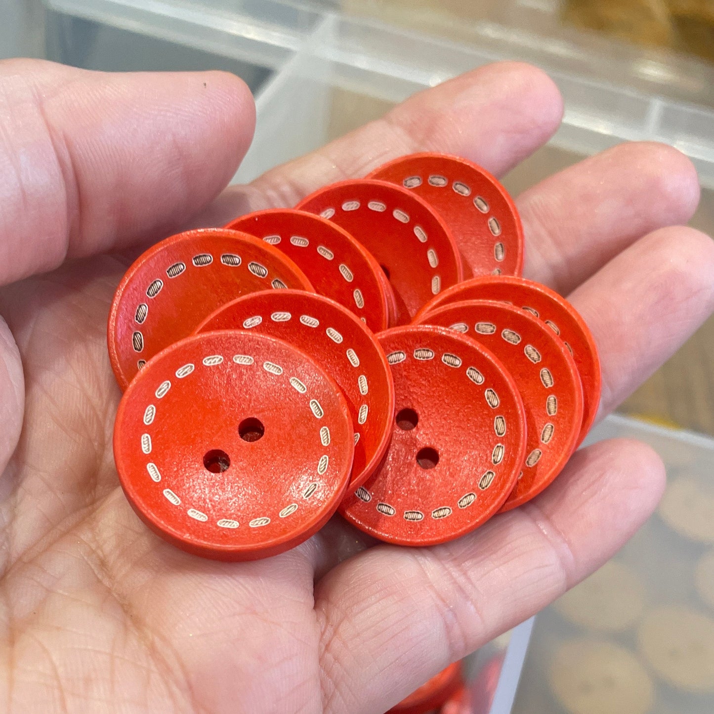 Hand holding red buttons with a container of buttons in the background