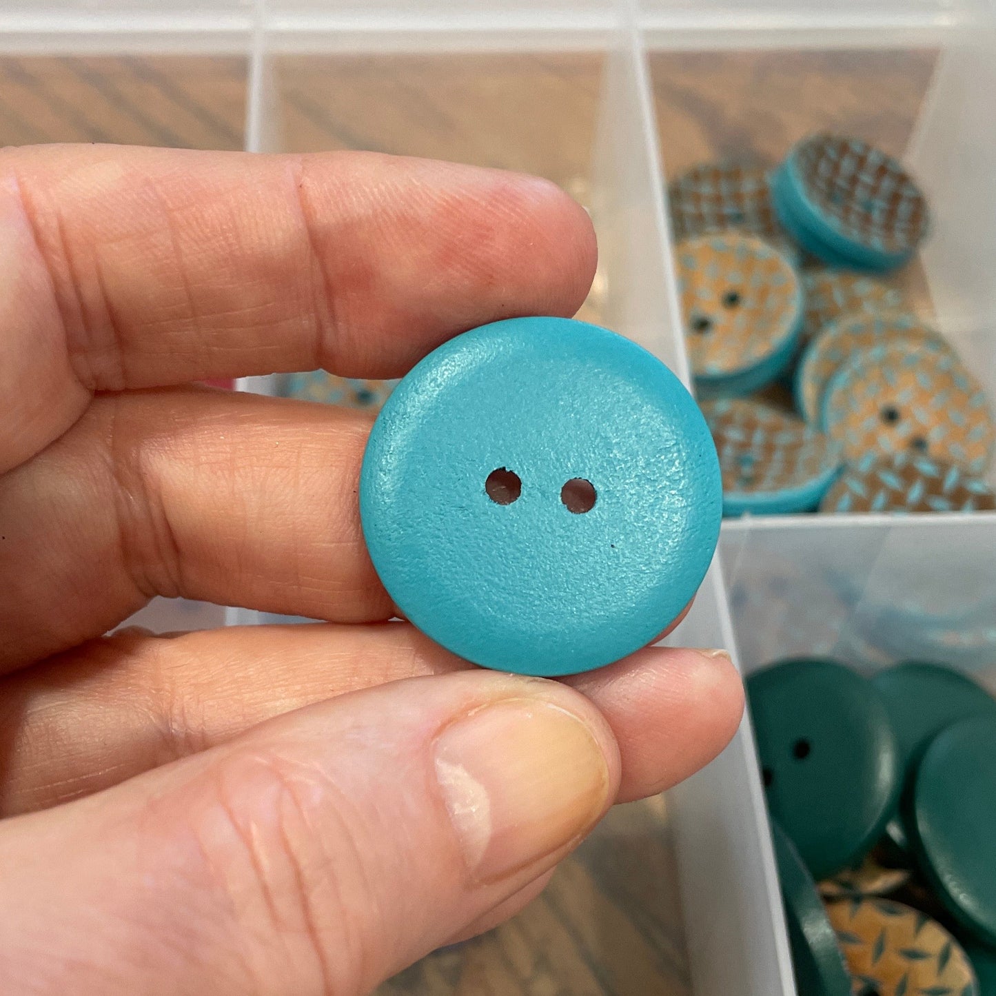Hand holding a blue button with a container of buttons in the background