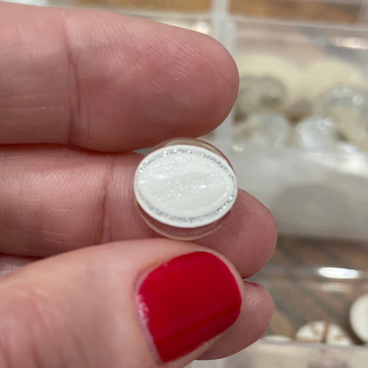 Close-up of a hand holding a white button with a clear container of buttons in the background.