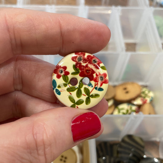 Hand holding a floral button with a container of buttons in the background