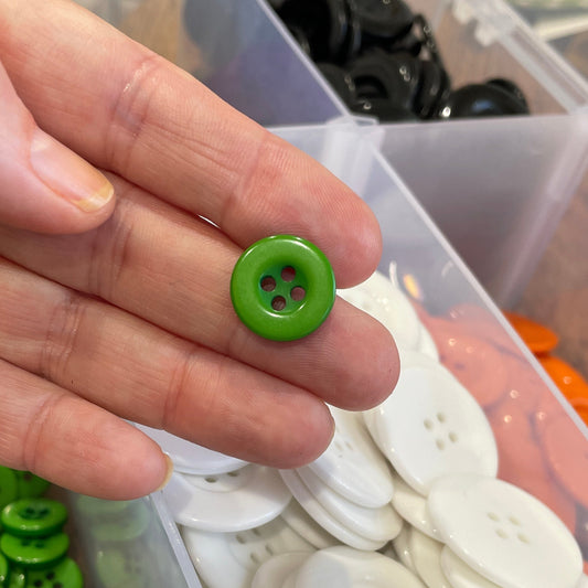 Hand holding a green button with a container of buttons in the background