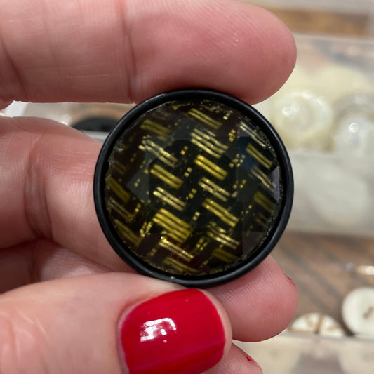 Close-up of a hand holding a small round object with a textured surface, with a blurred background of a container with beads.