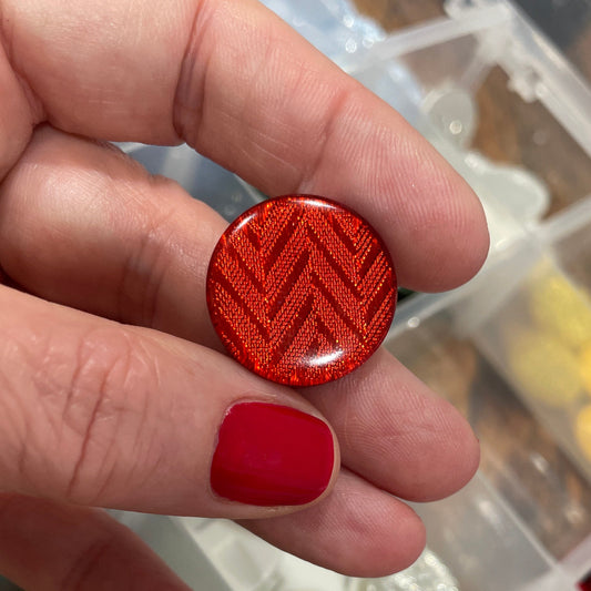 Hand holding a red textured button with a container of various buttons in the background
