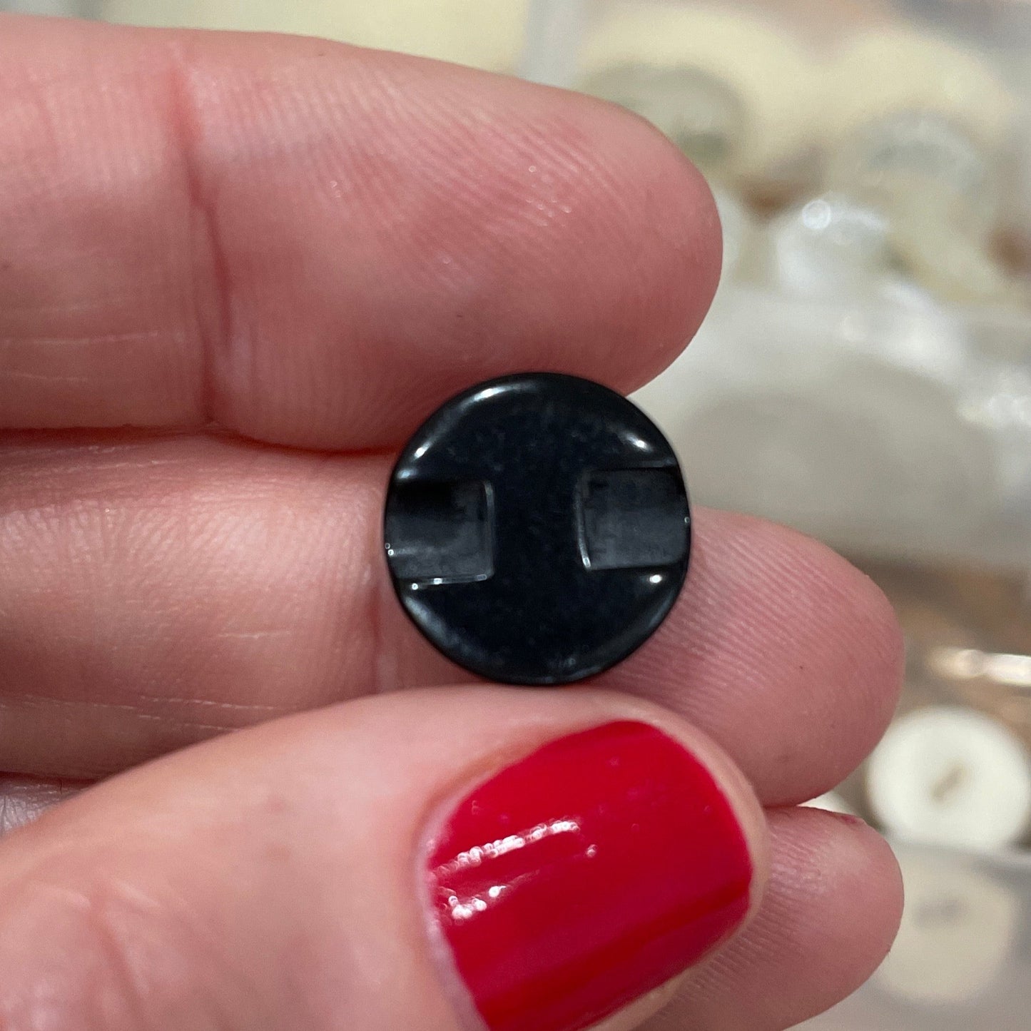 Black button held between fingers with a container of buttons in the background