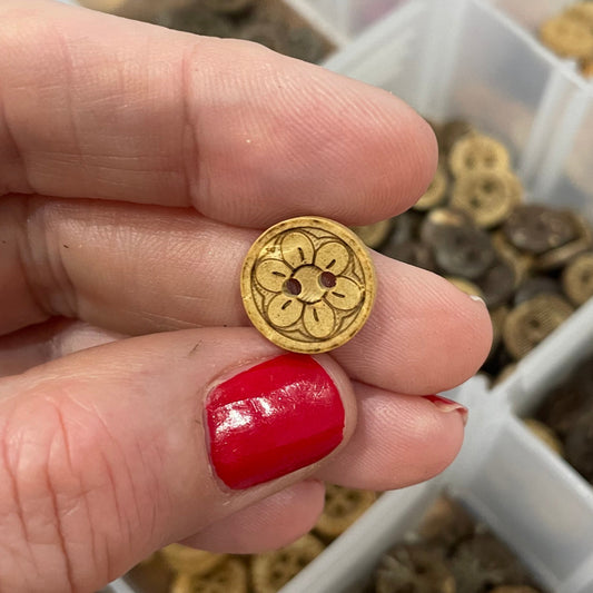 Button held by a hand with red nail polish, against a background of button assortment.