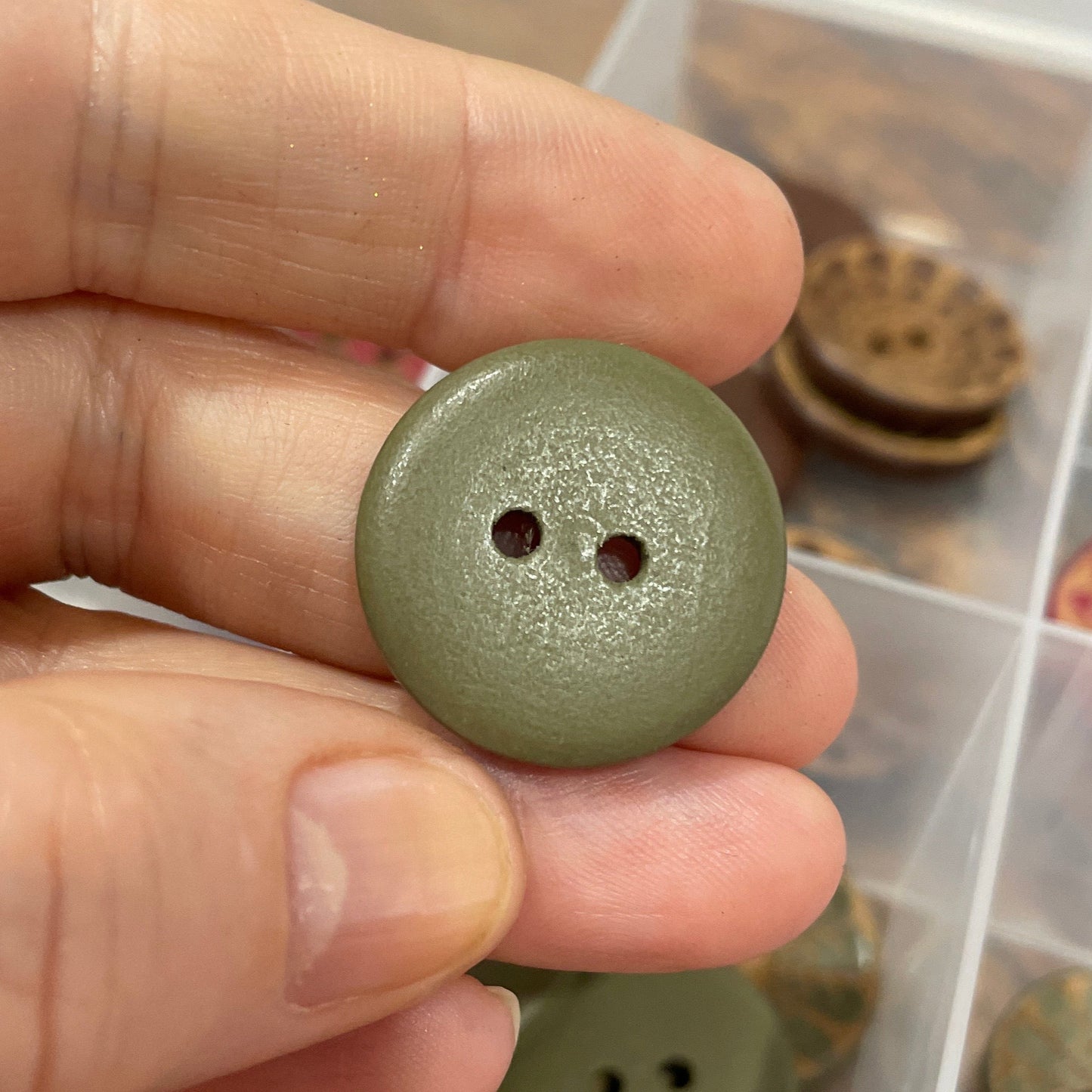 Hand holding a green button with a collection of buttons in the background