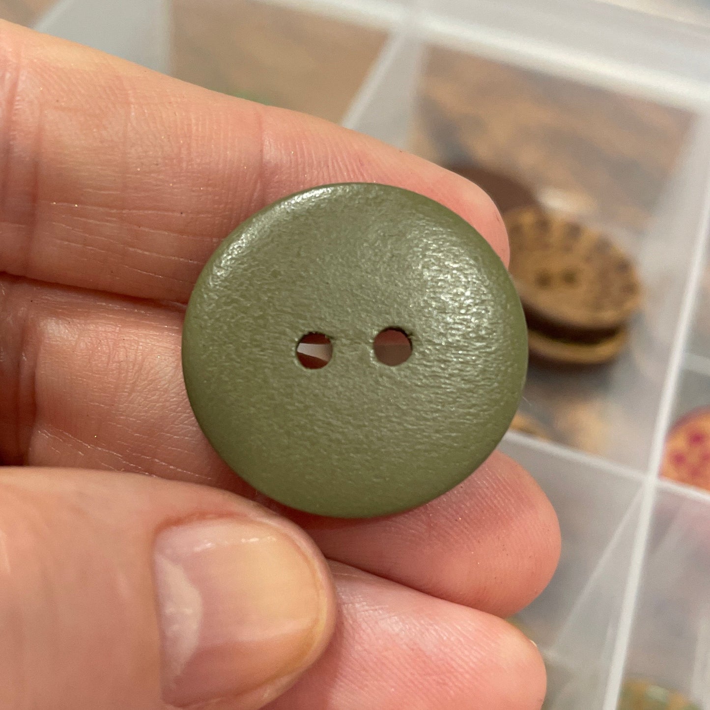 Green button held by a hand with a container of buttons in the background