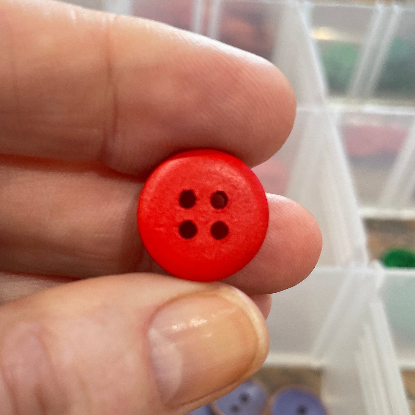 Hand holding a red button with a background of various buttons in a box.