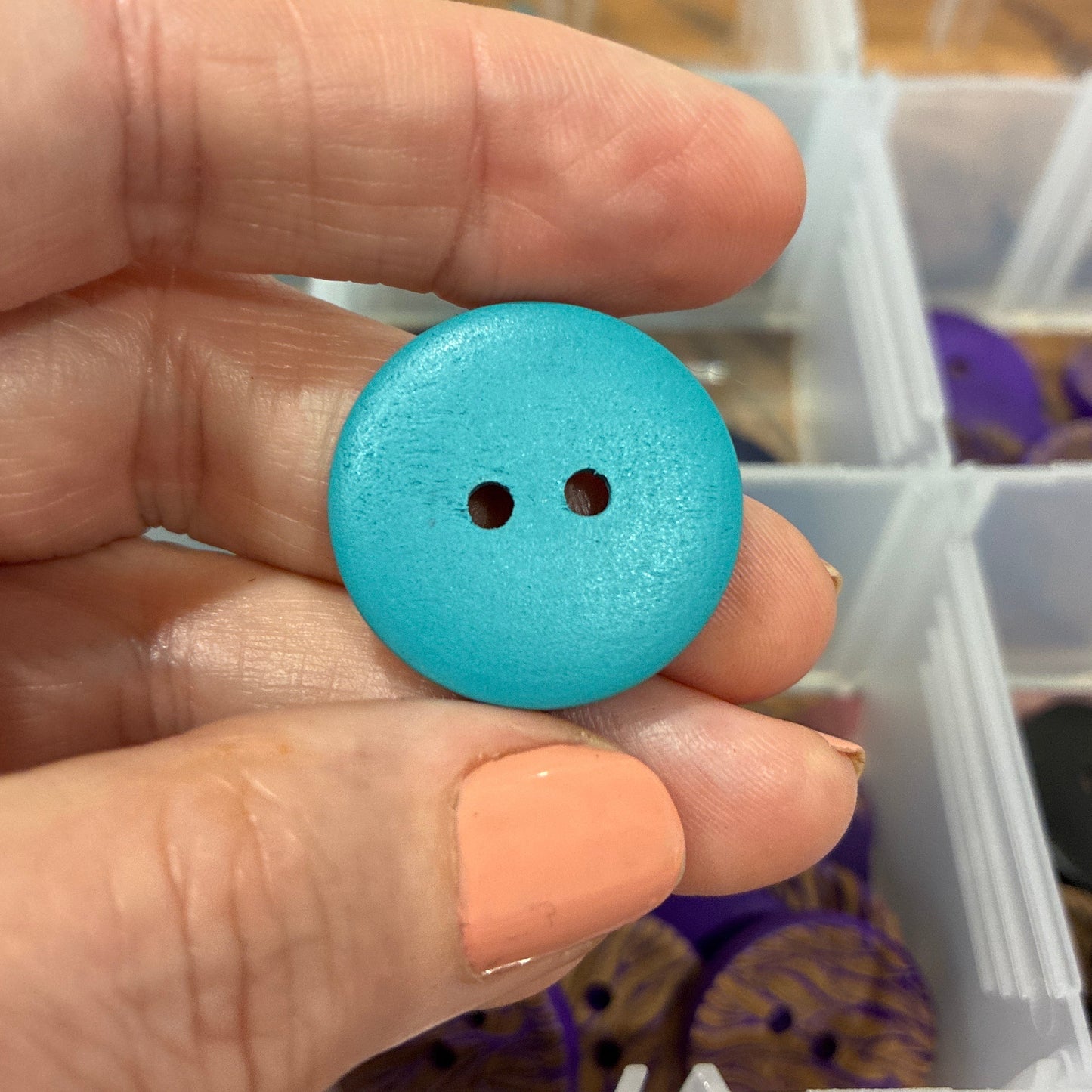 Hand holding a blue button with a background of various buttons in containers.