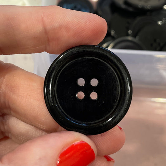 Hand holding a black button with a clear container of buttons in the background