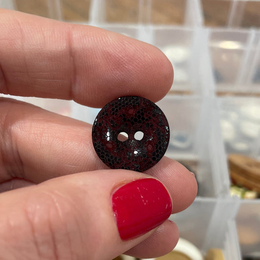 Hand holding a button with a clear container of buttons in the background