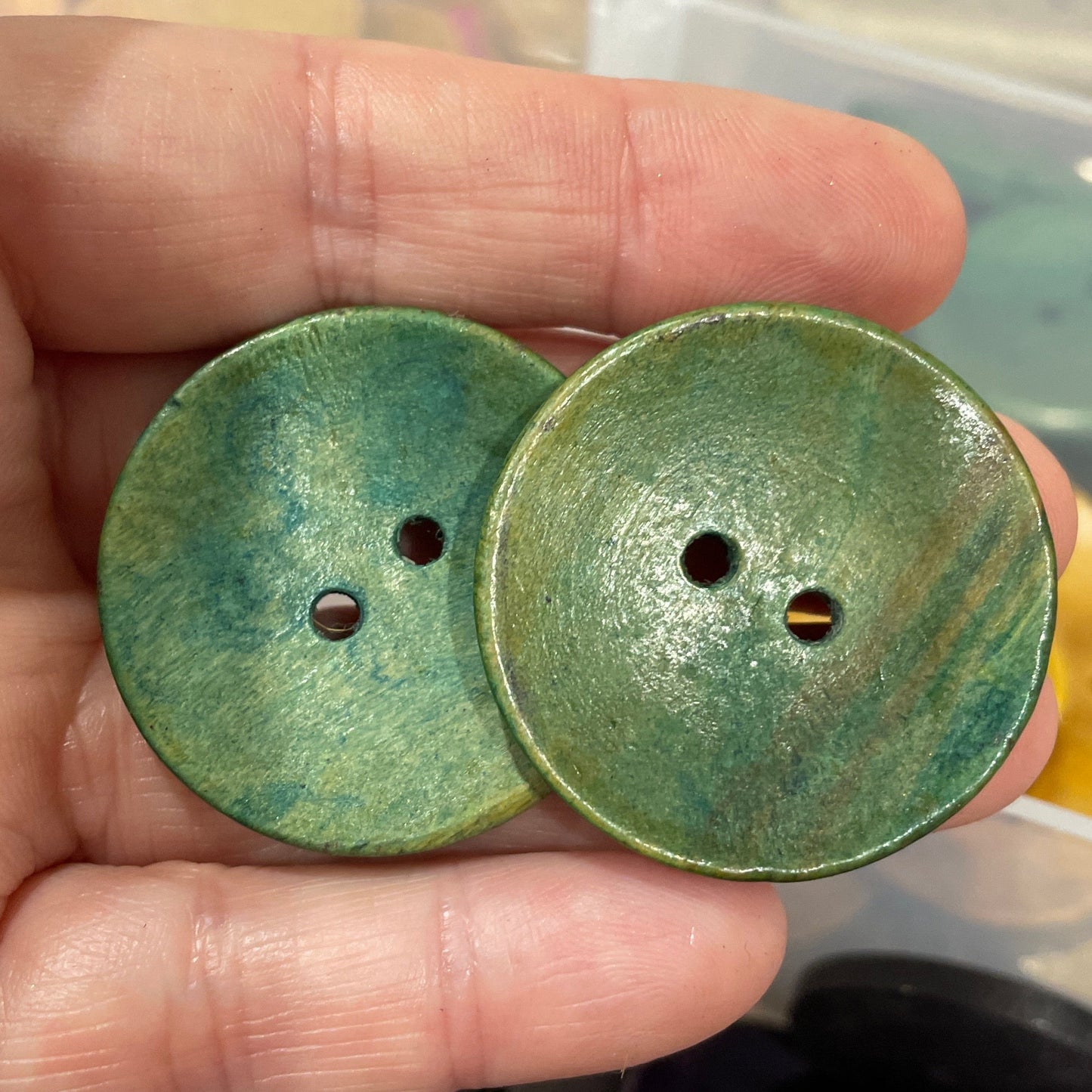 Green buttons held in a hand with a blurred background of more buttons.