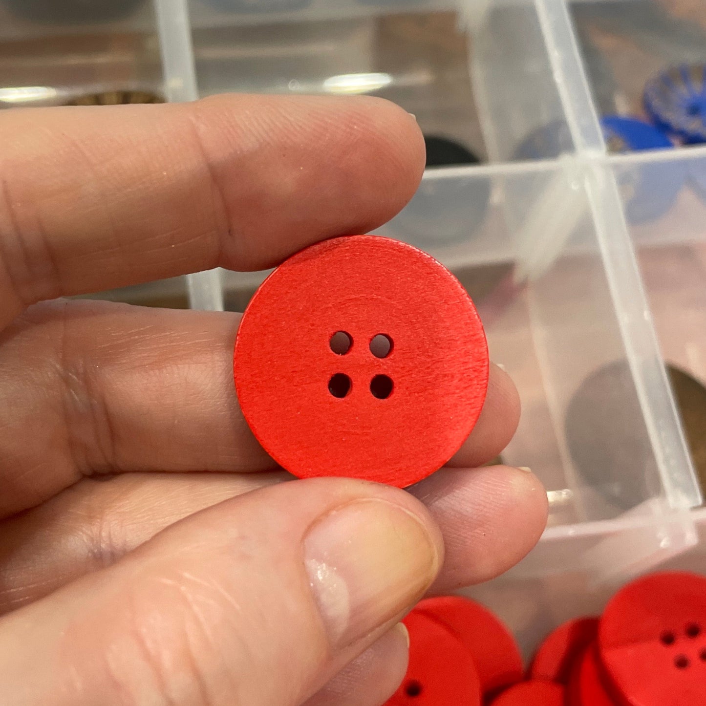 Red button held by a hand with a container of buttons in the background
