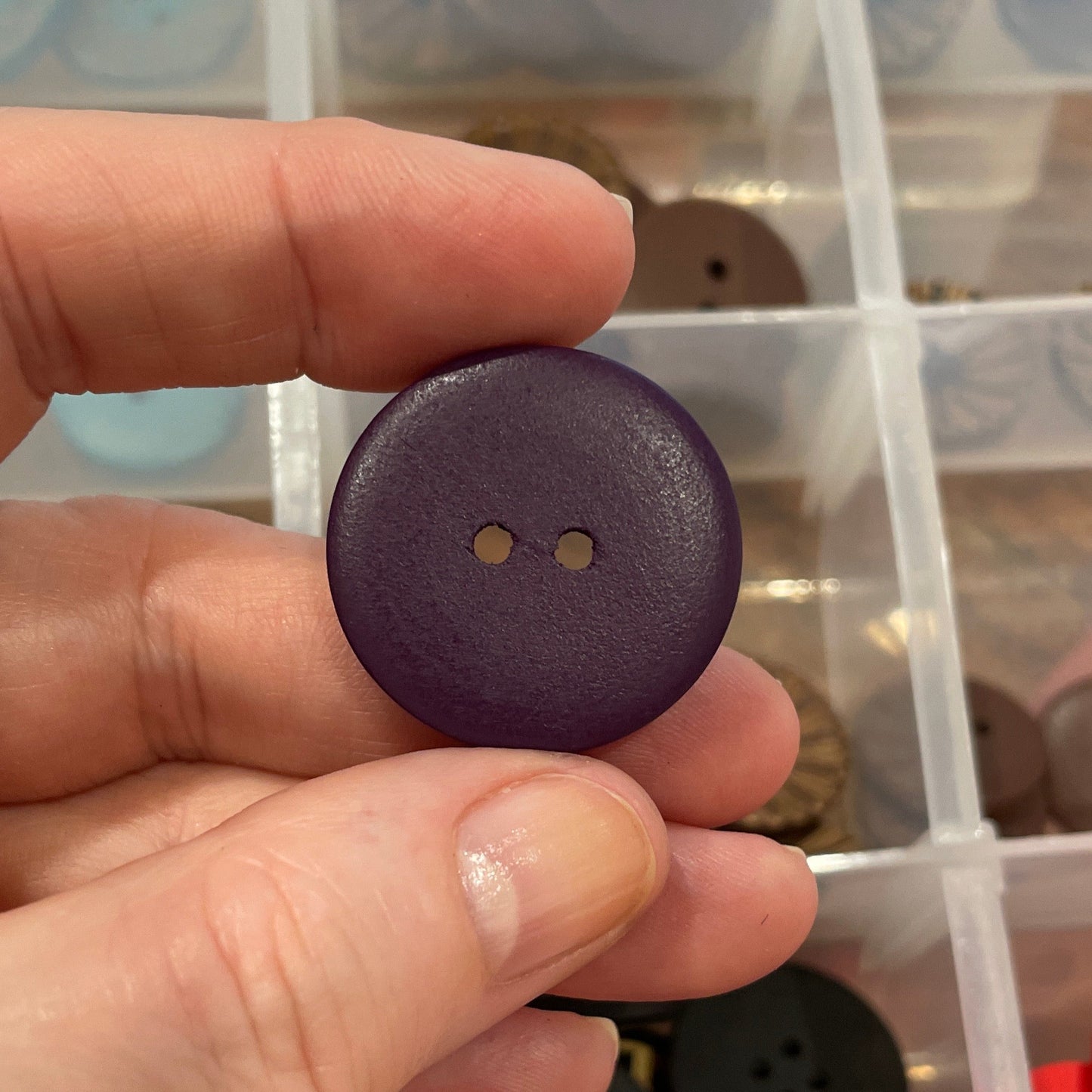 Hand holding a purple button with a clear container of buttons in the background