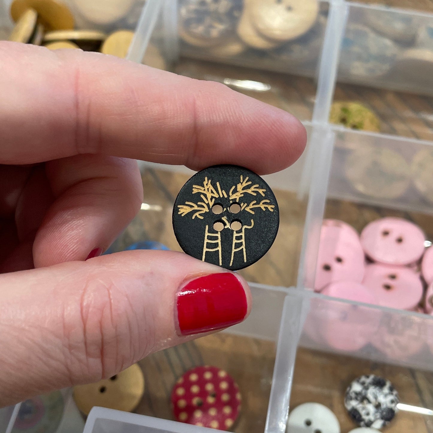 Hand holding a black button with gold design in front of a container of various buttons.