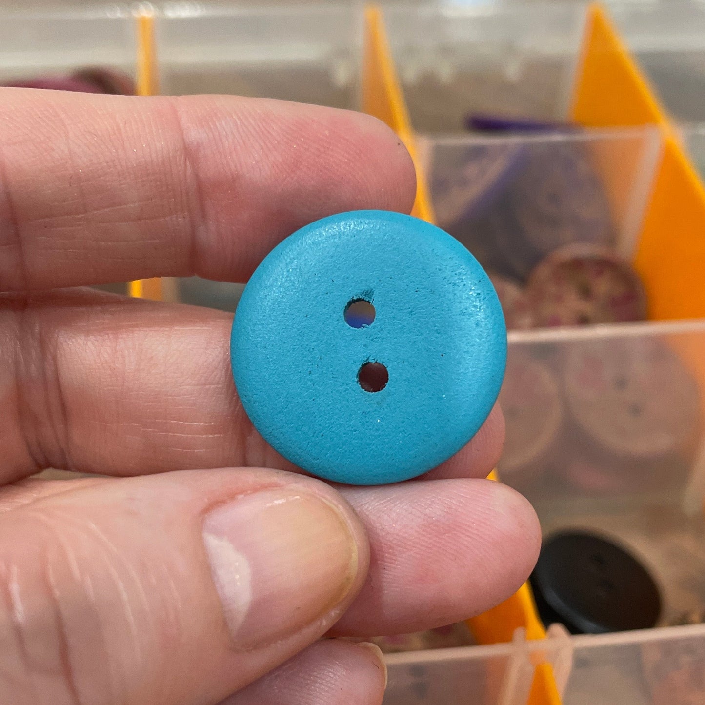 Hand holding a blue button with a background of button containers.