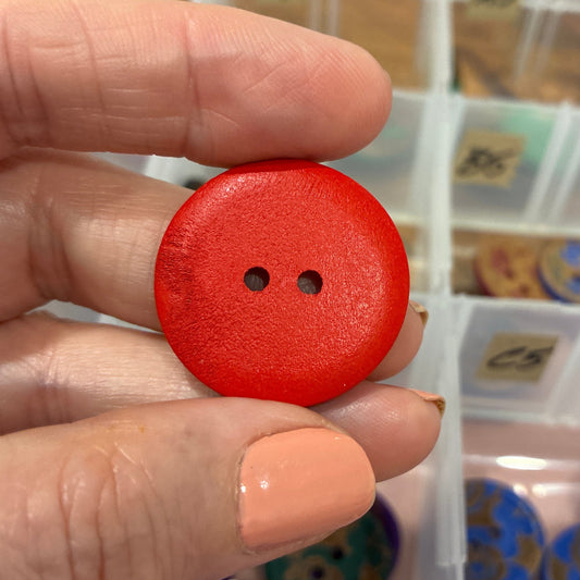 Hand holding a red button with a blurred background of a button organizer.