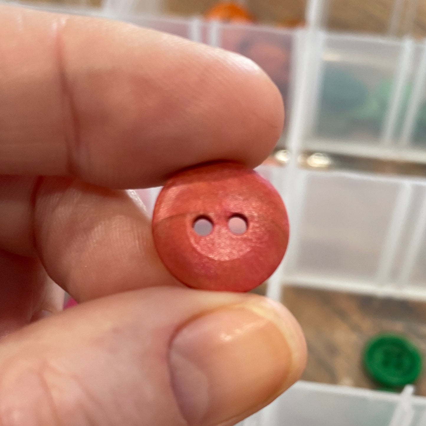 Person holding a red button with a clear container of assorted buttons in the background