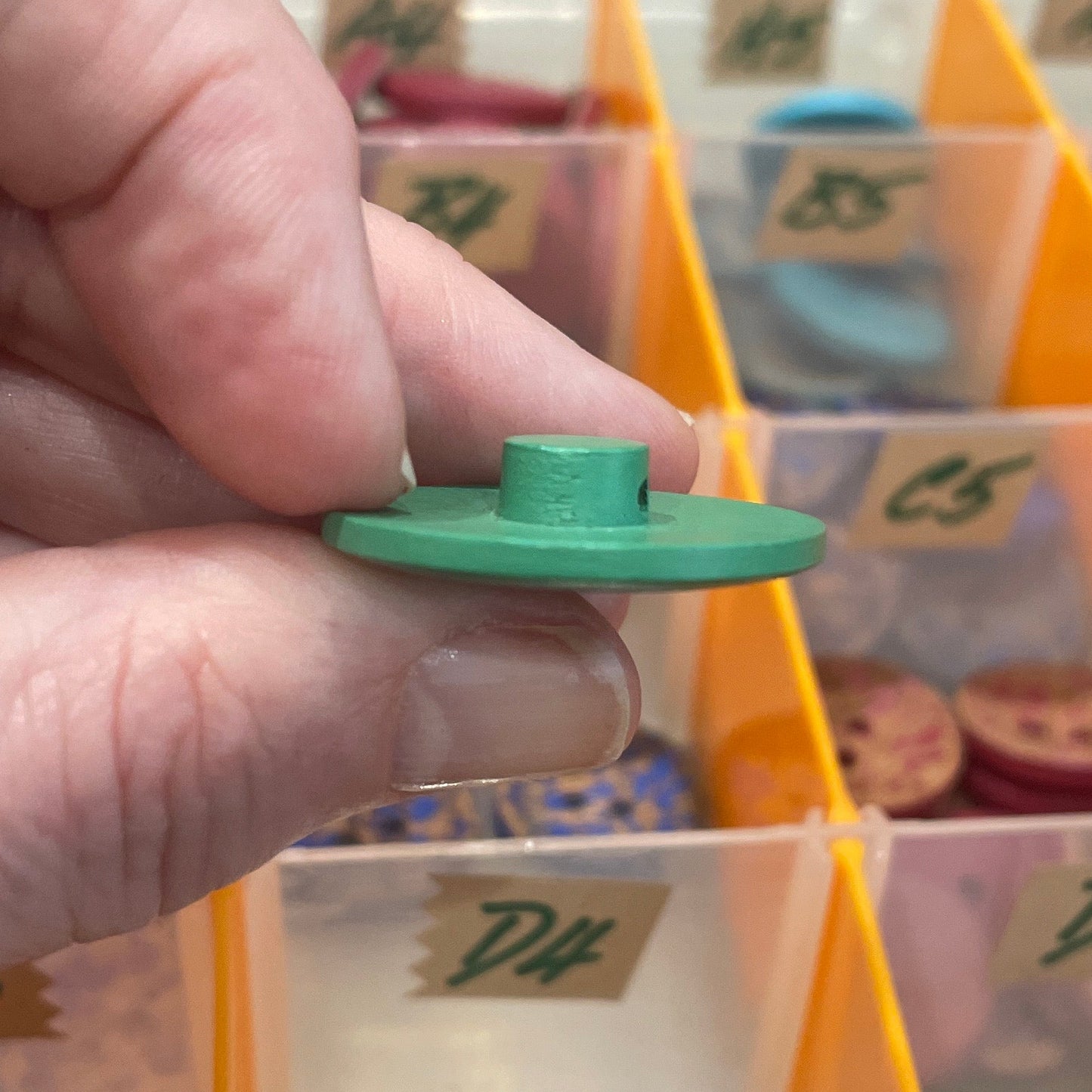 Hand holding a green button in front of a container of buttons
