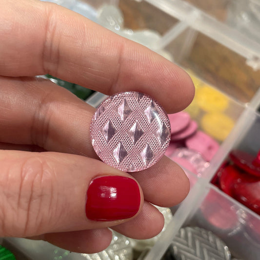 Hand holding a patterned button with a container of buttons in the background