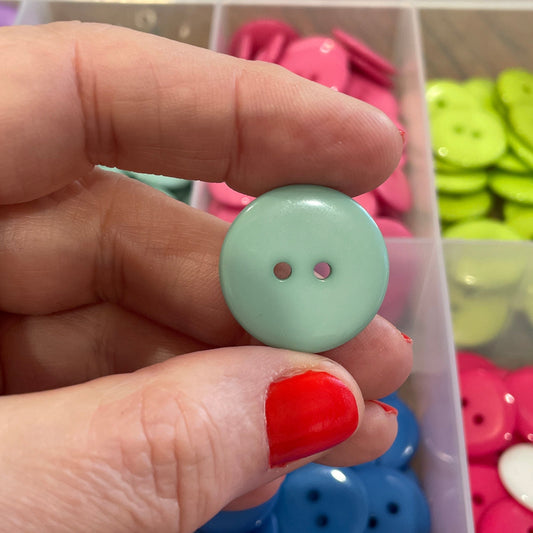 Hand holding a light green button with a colorful button collection in the background