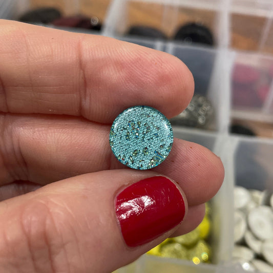 Blue textured round object held between fingers with a blurred background of colorful items.