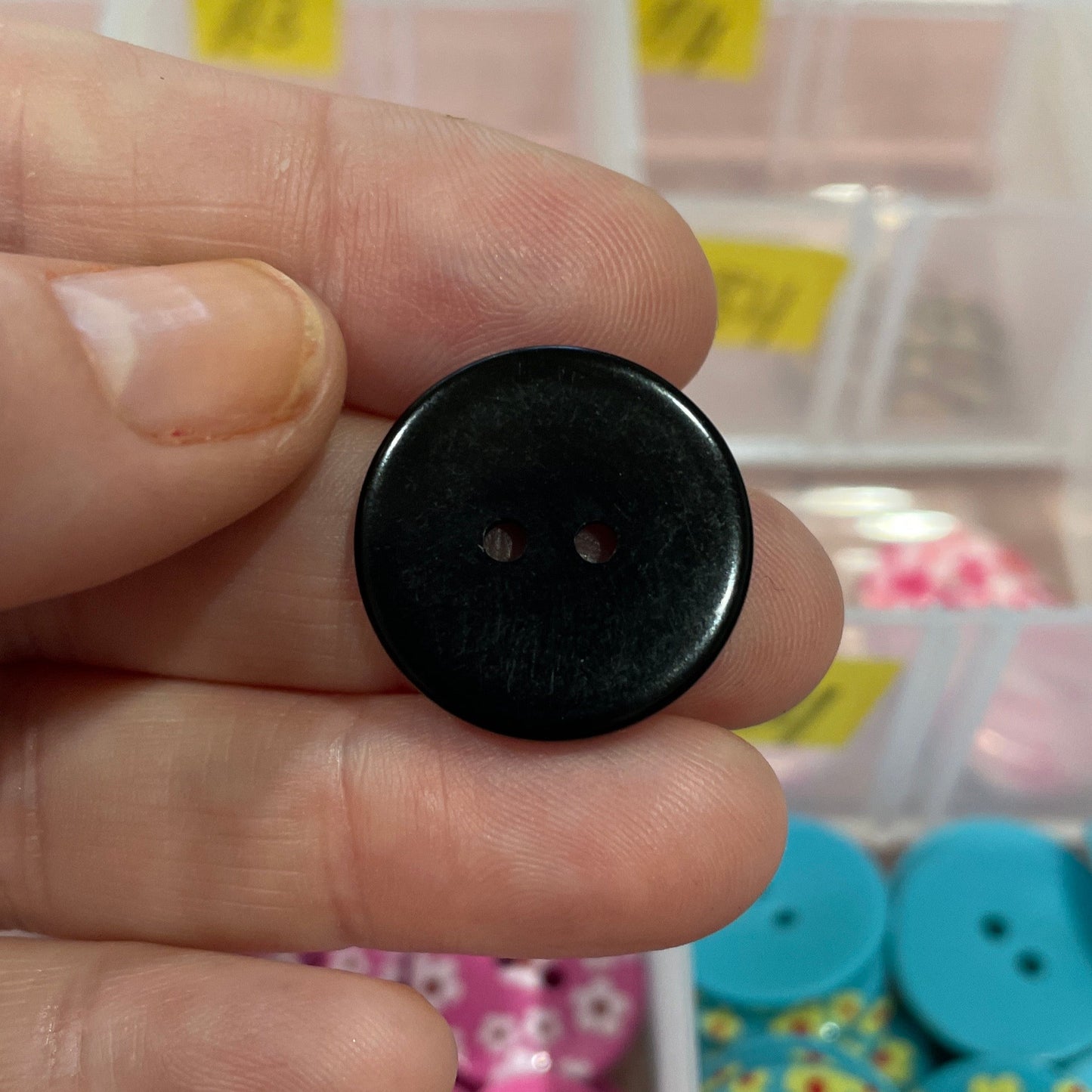 Black button held between fingers with a colorful button collection in the background
