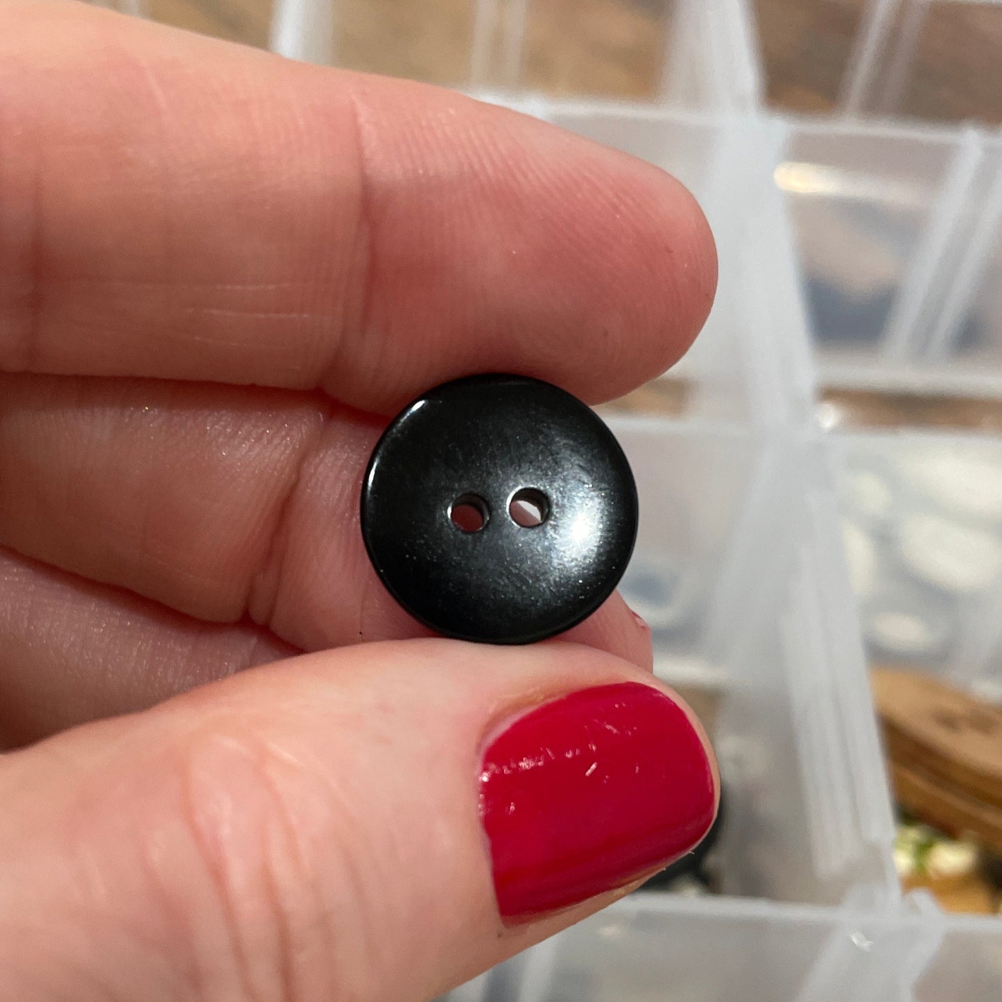 Black button held between fingers with a container of buttons in the background
