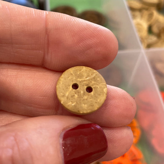 Gold button held between fingers with a container of colorful buttons in the background