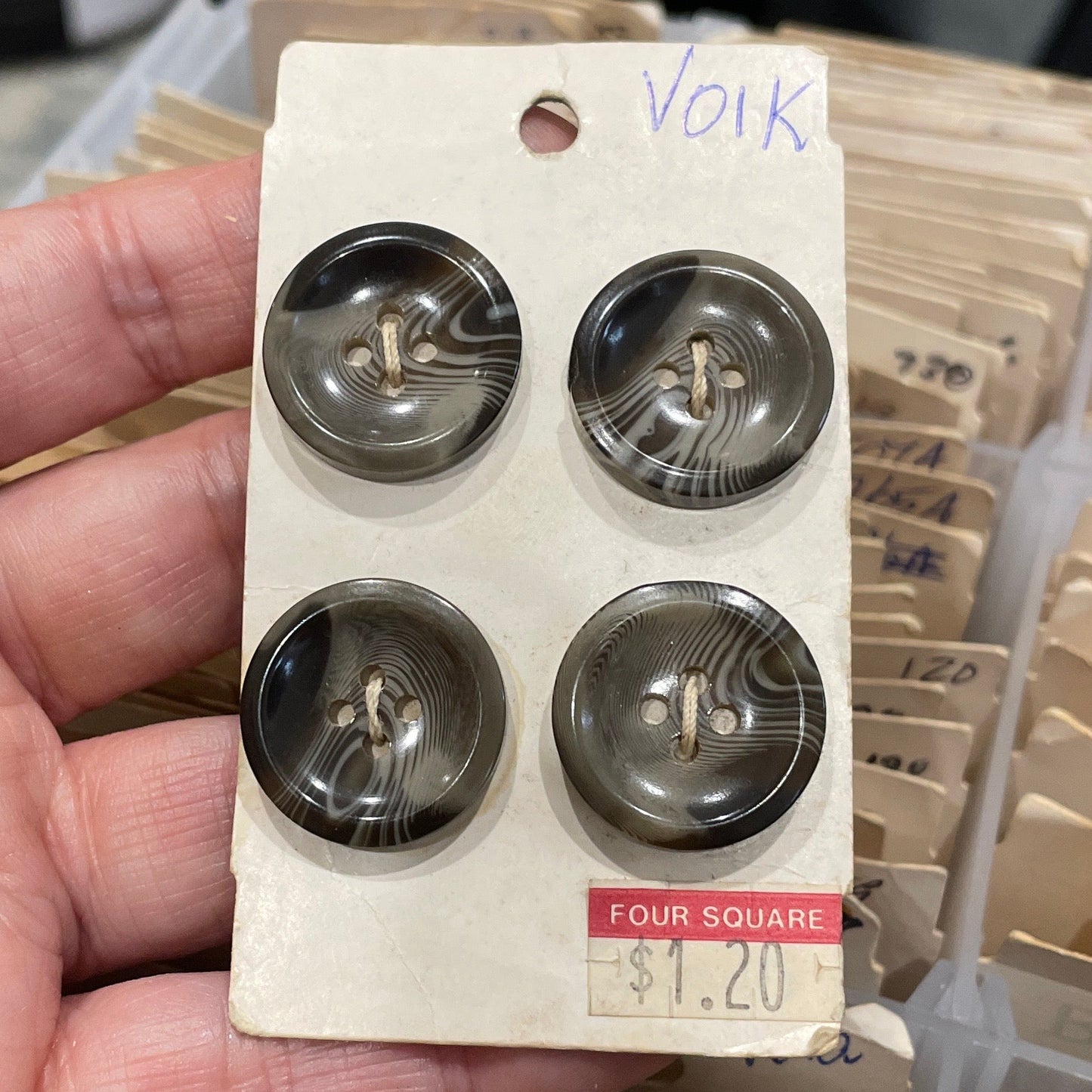 Hand holding a package of buttons with a blurred background of similar packages.