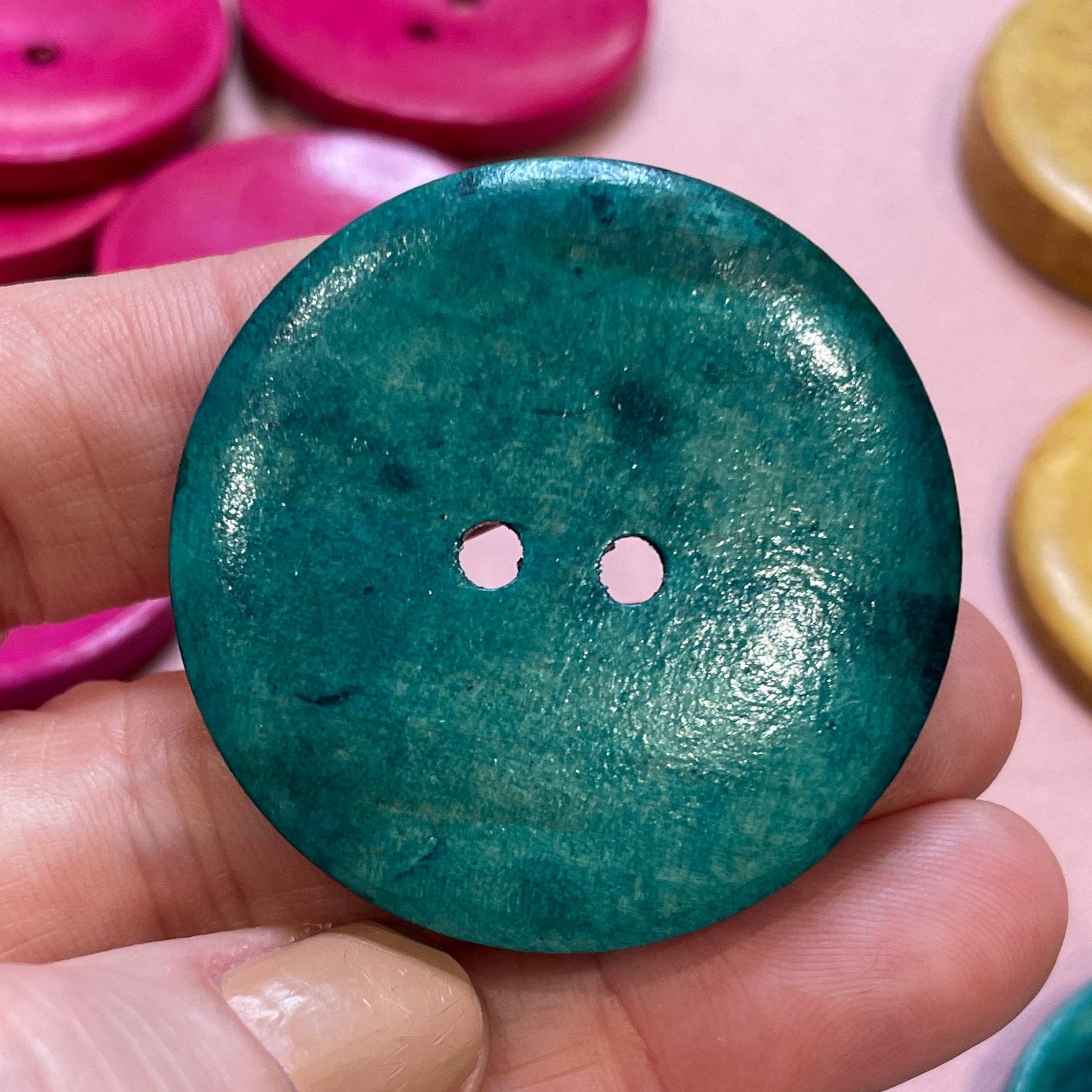 Hand holding a teal button with other colorful buttons in the background