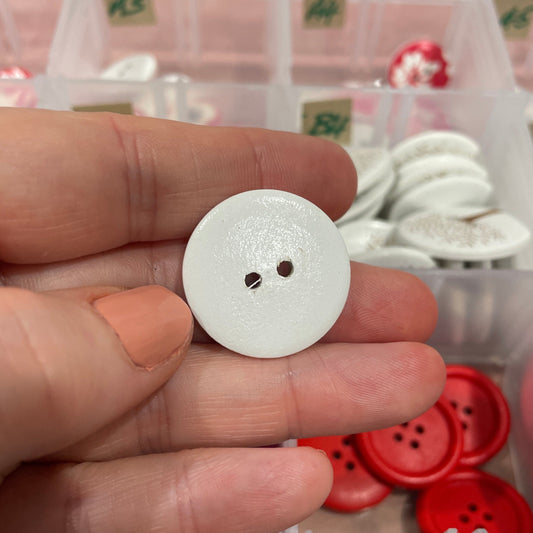Hand holding a white button with a background of various buttons in a box.