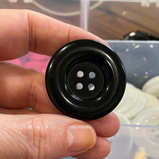 Black button held by a hand with a clear container of buttons in the background