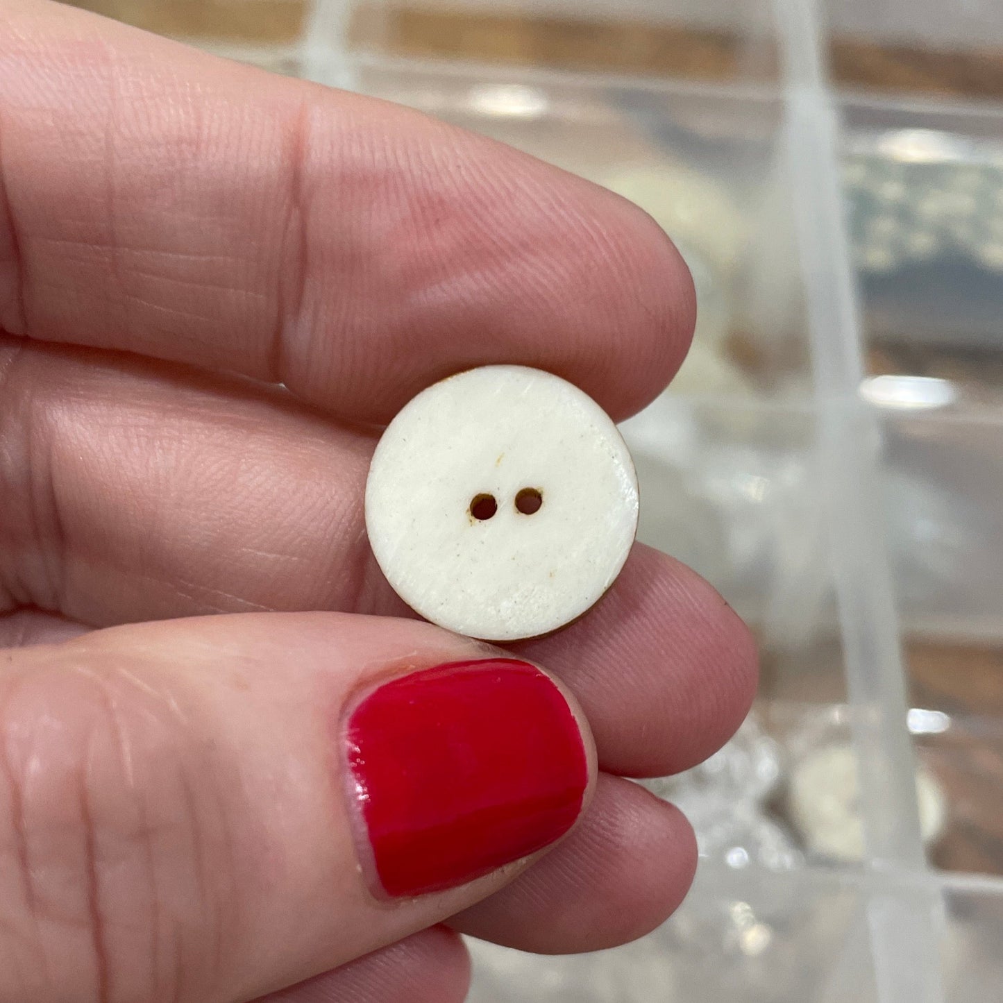 Hand holding a white button with a clear container of buttons in the background