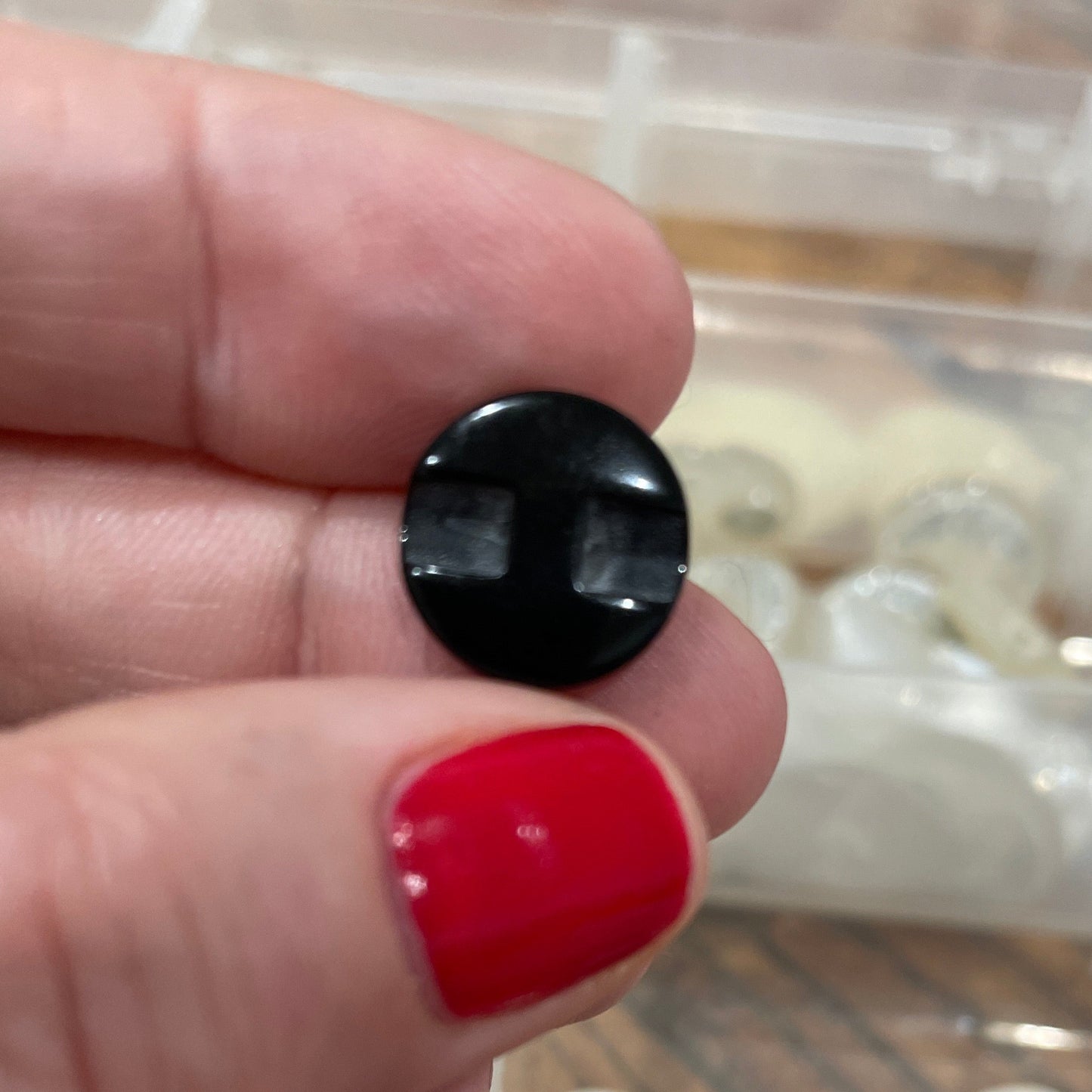 Hand holding a black button with a container of buttons in the background