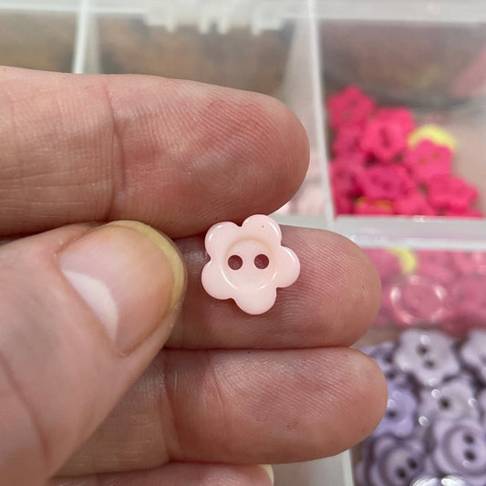 Hand holding a small pink button with a clear container of buttons in the background