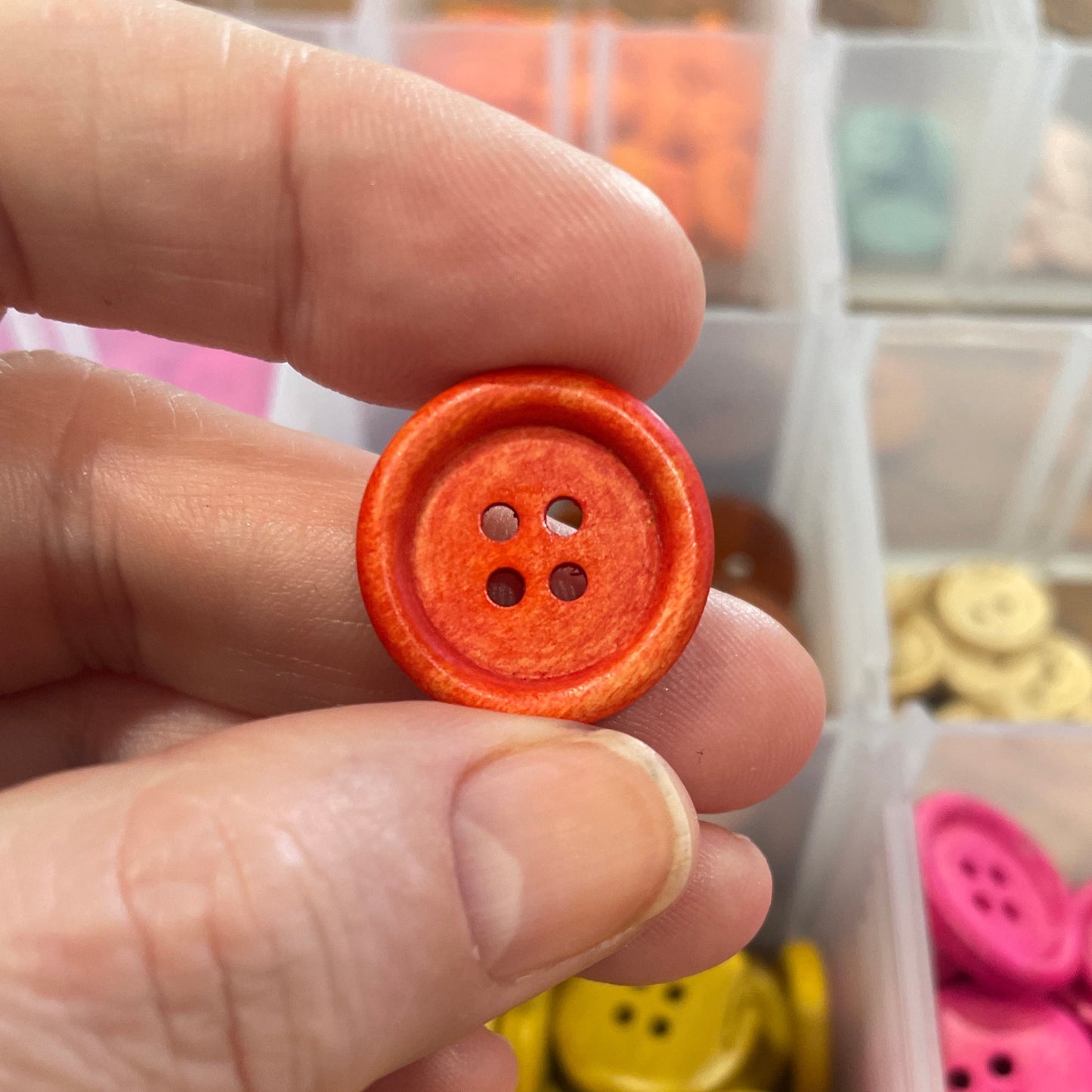 Hand holding an orange button with a container of colorful buttons in the background
