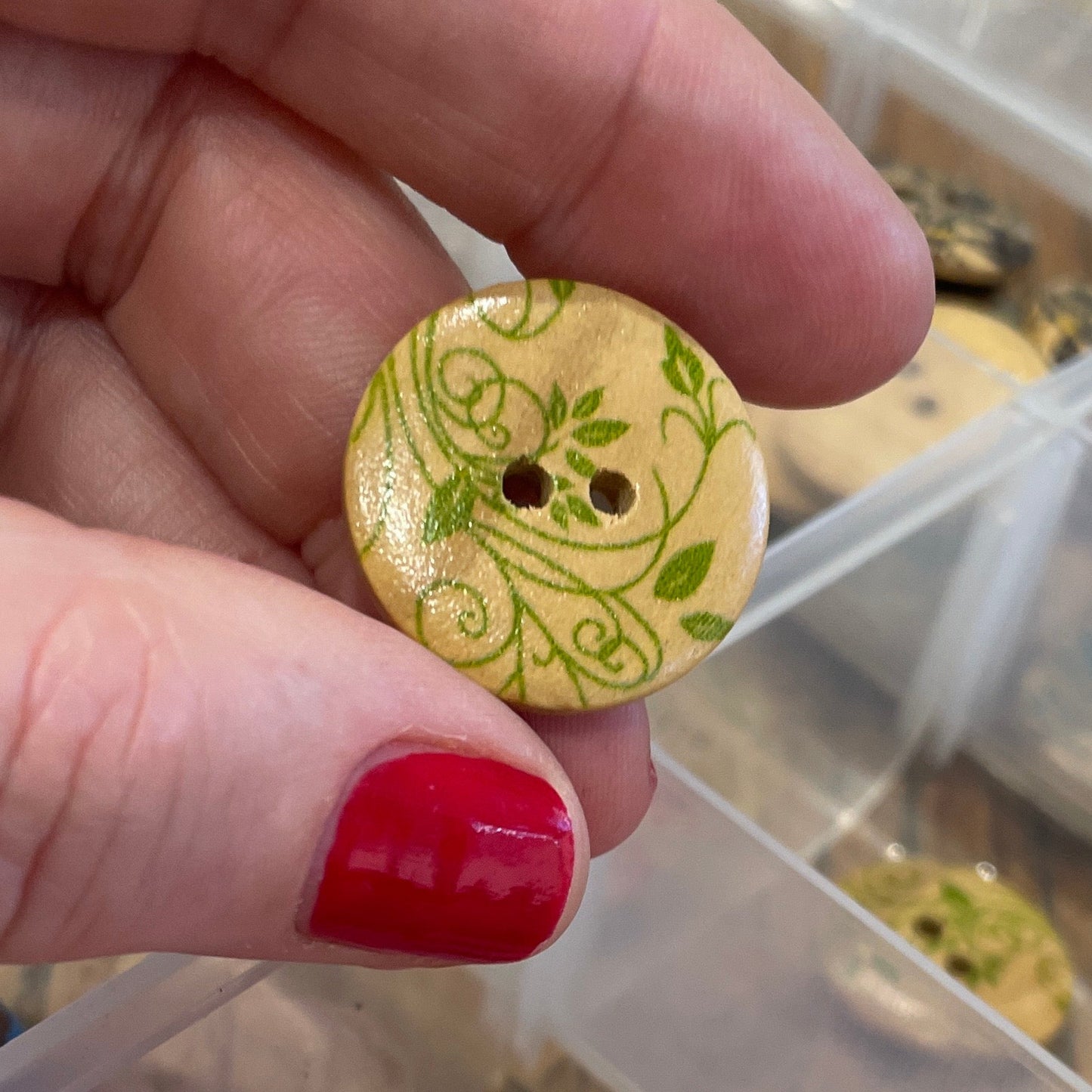 Hand holding a decorative button with a container of assorted buttons in the background.