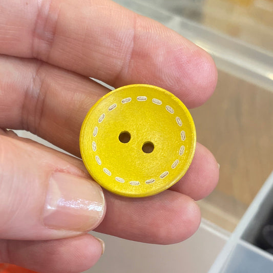 Hand holding a yellow button with a container of buttons in the background