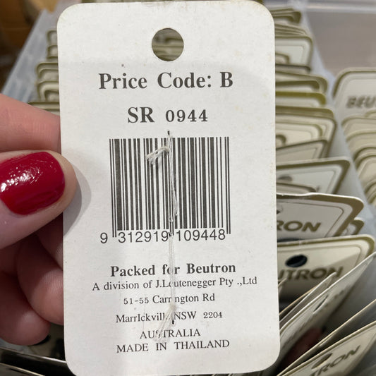 Close-up of a clothing tag with a barcode and text, held by a hand with red nail polish.