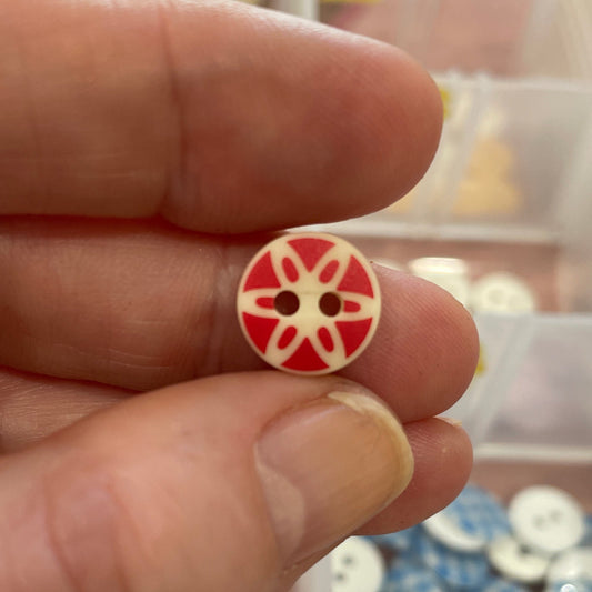 Hand holding a red and white button with a star design against a background of organized buttons.