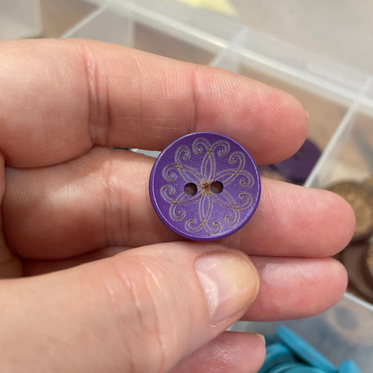 Hand holding a purple button with a container of buttons in the background