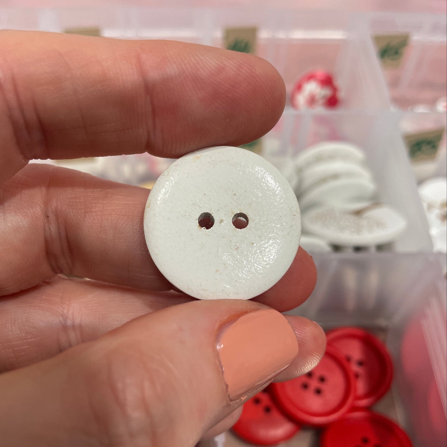 White button held between fingers with a blurred background of button collection